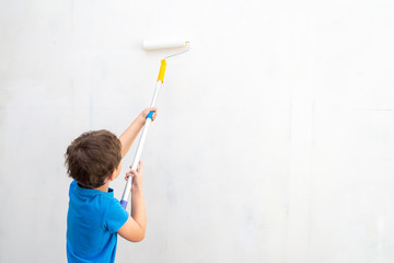 child rolls the roller in the paint on the wall. finishing work in the premises of the artist paints the walls. repair of premises, premises of the house. the child helps to paint the walls.copy space