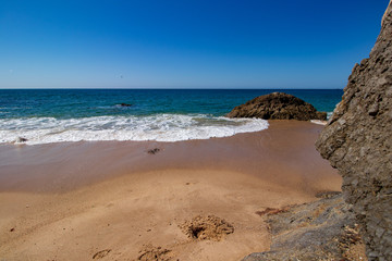 Sand, rocks, white foam and blue sky on the beach