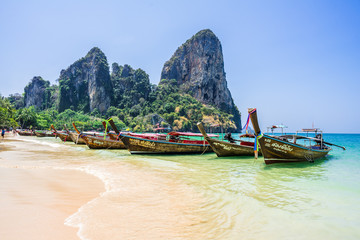 Fototapeta premium Longtail boats moored near the Railay Beach, Krabi / Thailand. Mountains with trees on the background. Clean blue sky