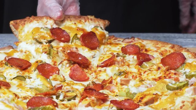 Close-up of chef's hands in silicone gloves taking a piece of delicious fresh Neapolitan pizza with circles of saveloy and cheese. Frame. Italian food