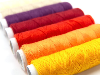 row of sewing threads in yellow, orange, red and purple isolated on white background