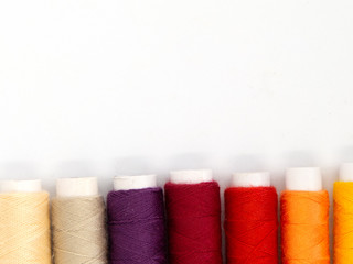 row of sewing threads in yellow, orange, red and purple isolated on white background