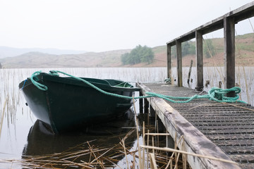 Obraz premium Zielona łódź wiosłowa przywiązana liną do drewnianego pomostu na jeziorze Loch w Argyll w Szkocji