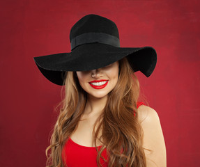 Happy cheerful model woman in black hat on red background. Smiling girl portrait