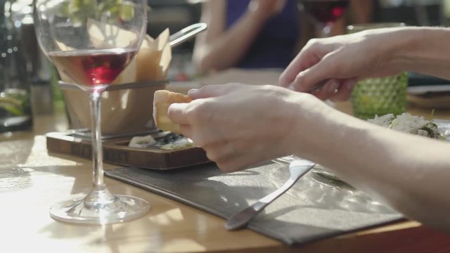 Young woman smearing on bread delicious cheeses and sauces from beautifully served plate in restaurant. Close up.