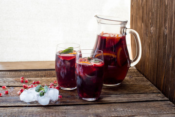Refreshing homemade lemonade with ice, pomegranate, orange and mint. on a wooden table.