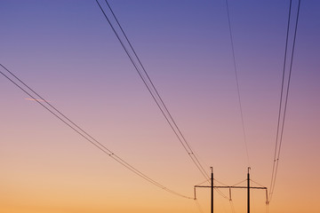 electrical wires against the dawn sky, in the background two pillars, focusing on the wires, concept