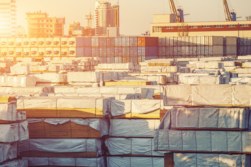 Outdoor storage in freight port with pallets, stacks and containers of building material goods for construction at sunset. Shipping and logistics concept