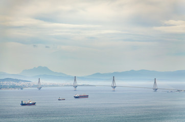 View of the suspended Rio Antirrio bridge with ships passing on a cloudy day