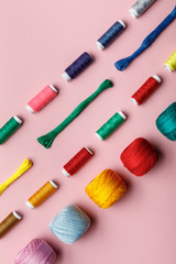 top view of colorful knitting yarn balls, embroidery threads and thread coils on pink