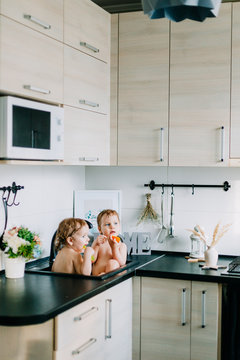 two twin girls bathing in the kitchen bathroom. play, wash their heads, laugh with each other