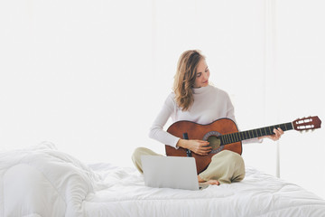 Beautiful young girl sitting playing guitar on bed in bedroom