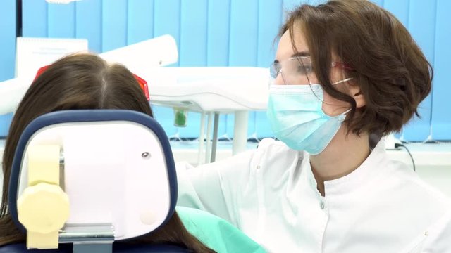 Rear view of the dentist treating teeth to woman patient in clinic, dental care concet. Media. Female professional doctor stomatologist at work with dental equipment.