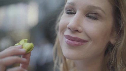 Portrait of pretty blond woman with curly hair eating green macaroon in the restaurant close up. The lady closing her eyes showing great pleasure