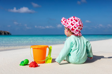 Baby sitzt am Strand und spielt mit seinen bunten Spielsachen im Sand