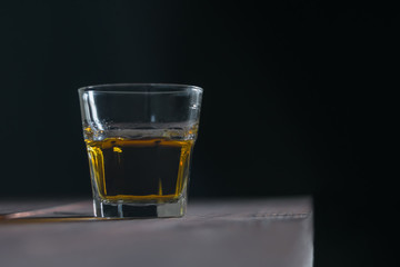 Glass of whiskey on the edge of the table on a dark background