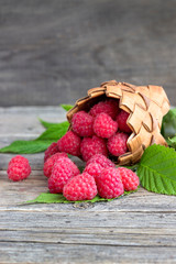 Ripe raspberries in a basket on a wooden background.