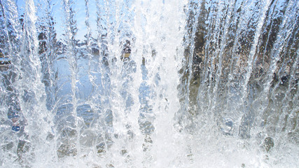 Transparent blue white water pours from above. View through the water wall of the waterfall for the...
