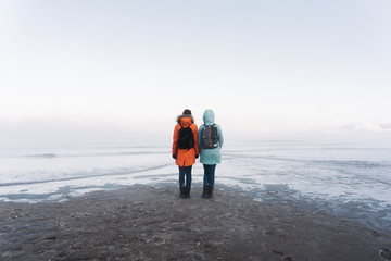 two girls in bright jackets are standing on the seashore during the outflow of water in the winter in severe frost in the far north