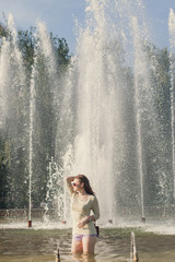 beautiful girl with flowing hair in short shorts and sunglasses is standing in the fountain