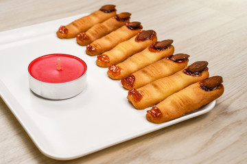Homemade backed spooky Halloween witch finger cookies covered with sweet cherry blood on a white plate with red candle