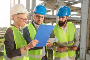 Small group of architects and civil engineers meeting on a construction site. Discussing future plans and looking at project documentation