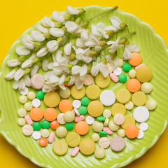 Fototapeta na wymiar allergy concept, on a green plate there are a lot of multi-colored tablets and a white acacia inflorescence