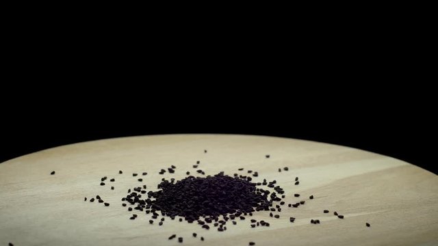 Cumin seeds rotates on a wooden board; isolated on a black background; closeup shot.