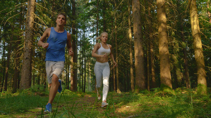 Naklejka na ściany i meble CLOSE UP: Happy woman and her boyfriend exercising by running through the woods.