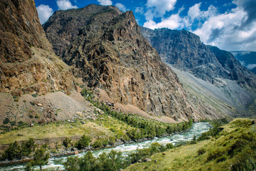 Fototapeta na wymiar River among the high mountains. Picturesque landscape of rocky Altai mountains and Chulyshman river. Mountain range, river, green coast, blue sky and white clouds.