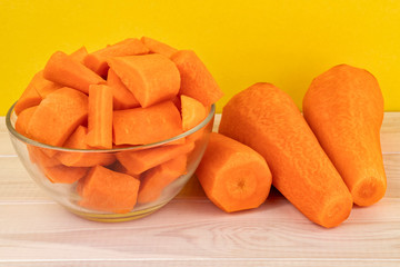 Fresh chopped carrots in a glass bowl on a yellow background