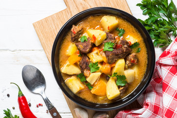 Goulash with meat and vegetables on white wooden table.