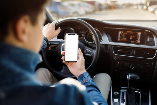 Young business man with phone in car. Man holding smartphone with blank screen .