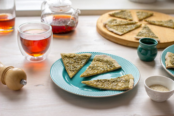 Italian flatbread focaccia with basil pesto sause and sesame seeds on a white table with tea