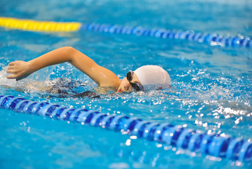 Young boy in goggles and cap swimming in the blue water pool