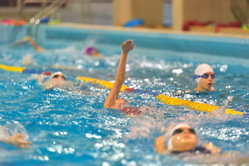 Young girl in goggles and cap swimming in the blue water pool