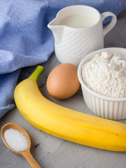 The ingredients for the banana cake on gray background. Wooden Spoon, Banana, Eggs, Milk