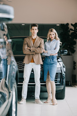 handsome man and beautiful blonde girl standing with crossed arms in car showroom