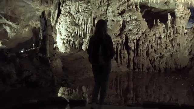 black silhouette woman with backpack,  tourist trip to Georgia,  stalactites, stalagmites Prometheus cave dark nature natural stone, excavations. Girl looks around wildlife, beauty elements rocks
