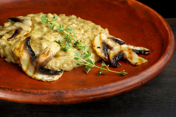 Wheat porridge with mushrooms on a black background in a clay plate.