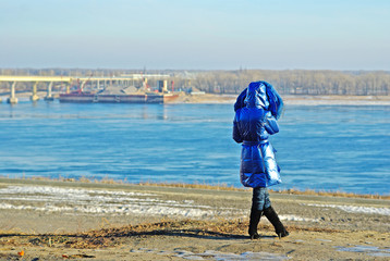 Rear view of woman in a blue coat standing on the bank of the river