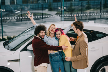 cheerful group of friends hugging with attractive blonde girl near white car