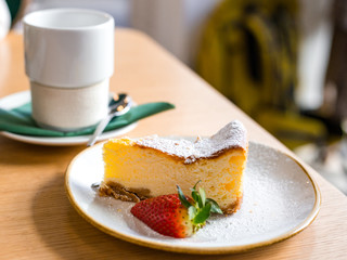 slice of cheesecake with strawberry on brown background, selective focus. A cheesecake pastry in a dish and coffee or tea cup.