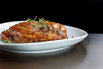 Roast pork knuckle on white plate, sprinkled with rosemary.