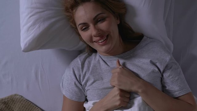 Happy woman lying in bed, looking at pregnancy test with positive result