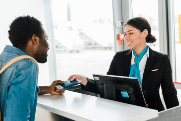 smiling african american airport worker giving passport and air ticket to tourist