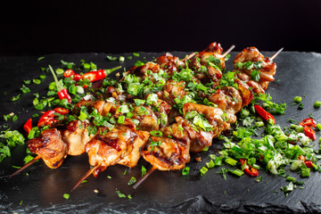 Grilled meat skewers, shish kebab on black slate. They lie close to each other.