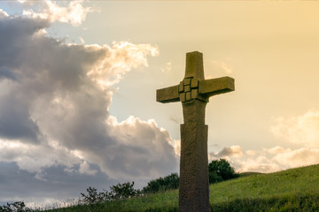 a stone cross in front of a dramatic evening sky