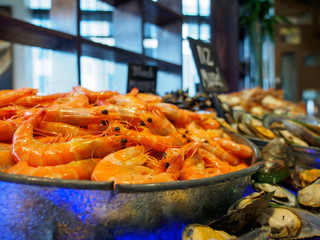 Wide closeup of a bowl of boiled banana shrimp chilled on ice next to New Zealand mussels at a hotel seafood buffet. Bangkok, Thailand. Travel and cuisine.