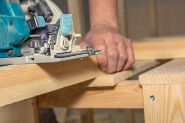closeup man works with handheld battery saw on wooden surface